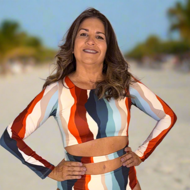 Woman in a colorful swimsuit standing on a sandy beach with palm trees in the background.